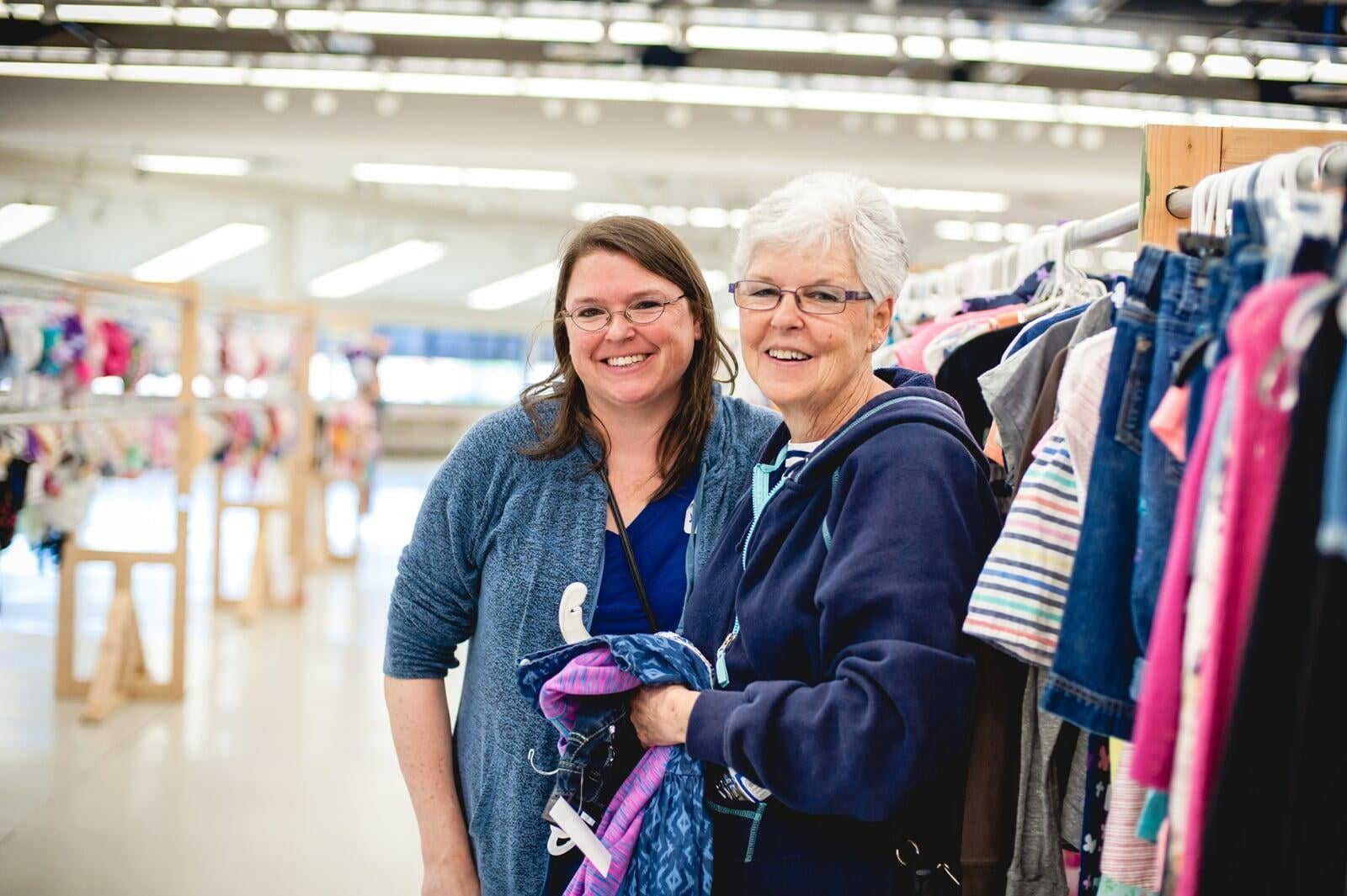 Mom and grandmother stand together, a few pieces of clothing in grandmom's hands, as they shop together for their family.